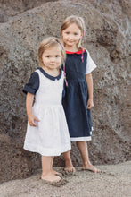Load image into Gallery viewer, Sofa Killer linen dark blue dress with red collar and white details, featuring two young girls posing on a rocky beach background, showcasing the stylish dress perfect for special occasions.
