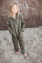 Load image into Gallery viewer, Unisex kids onesie by Sofa Killer in dark green, featuring a button closure, perfect for stylish mini-me outfits, worn by a young child standing on sandy ground.
