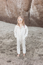 Load image into Gallery viewer, Sofa Killer linen beige unisex kids onesie worn by a child on the beach, showcasing a casual and stylish look with sunglasses.
