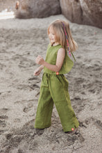 Load image into Gallery viewer, A young girl wearing the Sofa Killer linen moss green girl set, featuring a top and trousers, joyfully playing on a sandy beach.
