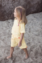 Load image into Gallery viewer, A side view of a child in the Sofa Killer linen yellow unisex set with shorts, walking on the sand. The outfit is made of soft linen, showcasing a stylish yet casual look ideal for outdoor fun.
