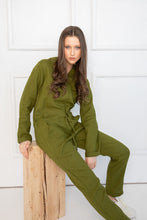 Load image into Gallery viewer, Sofa Killer moss green linen women onesie worn by a model sitting on a wooden block, showcasing its soft and comfortable fabric.
