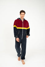 Load image into Gallery viewer, Model wearing the Sofa Killer Kansas velour onesie in dark grey, red, and yellow, showcasing a stylish and comfy look, perfect for lounging or casual outings.

