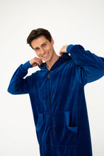 Load image into Gallery viewer, Sofa Killer men royal blue velour onesie Nevada, model smiling and adjusting the hood of a royal blue velour onesie, highlighting its cozy fit.
