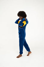 Load image into Gallery viewer, Side view of Sofa Killer women velour onesie Dakota in blue and yellow as a woman adjusts her hood, accentuating the comfy style.
