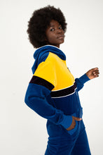 Load image into Gallery viewer, Close-up of the Sofa Killer men velour onesie Dakota, featuring vibrant yellow and royal blue colors, modeled by a person with an expressive look.
