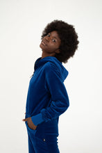 Load image into Gallery viewer, Close-up of a woman in a Sofa Killer royal blue velour onesie Nevada, featuring a confident smile and stylish hood.
